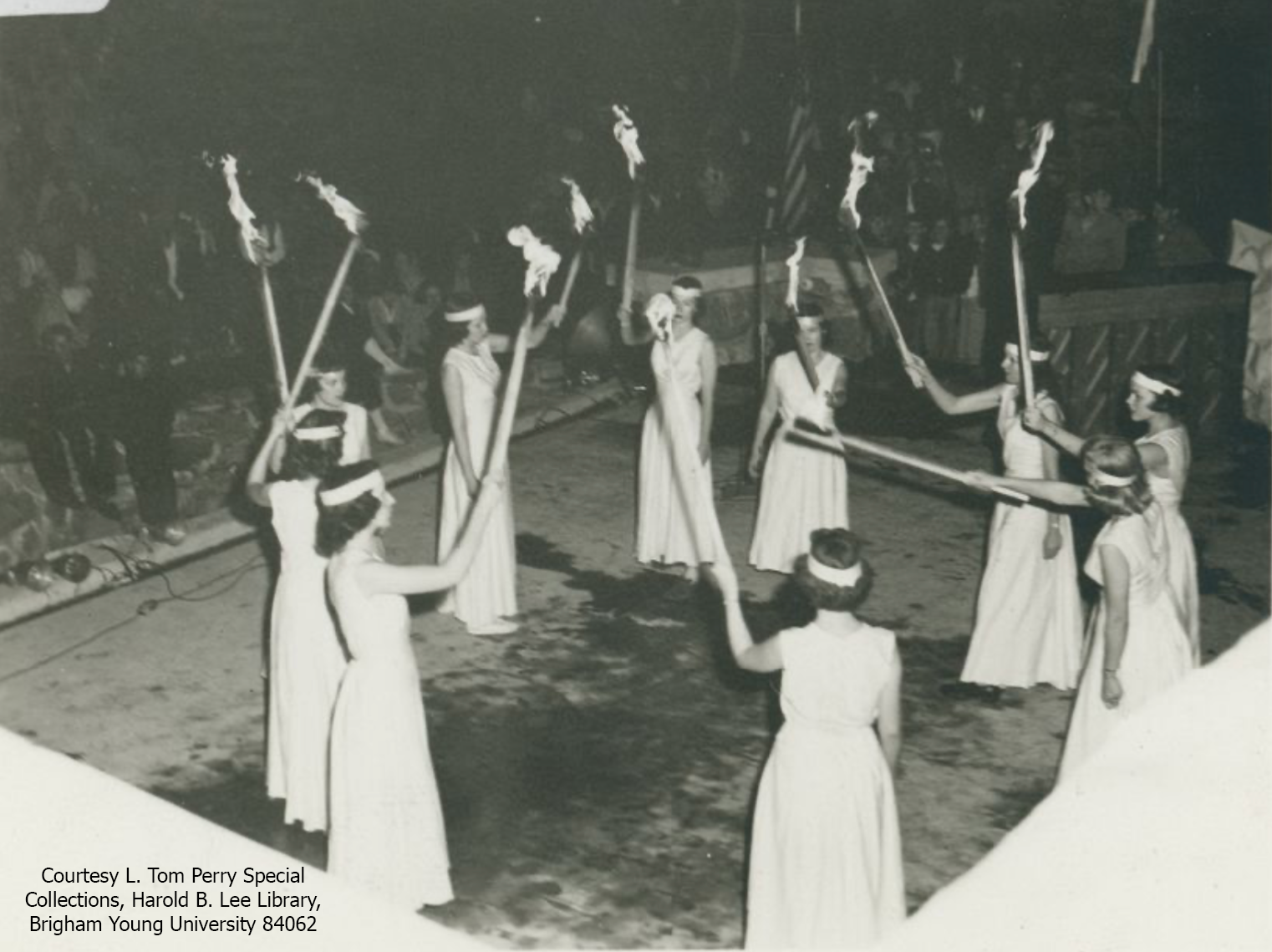 Young women dressed in white carry torches in this black and white photo