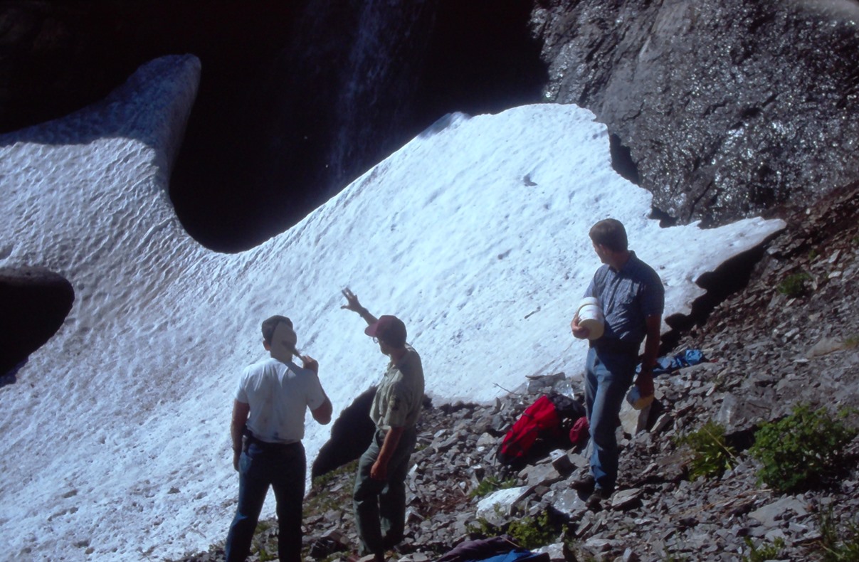 By a snowfield, people point to where they will place dynamite