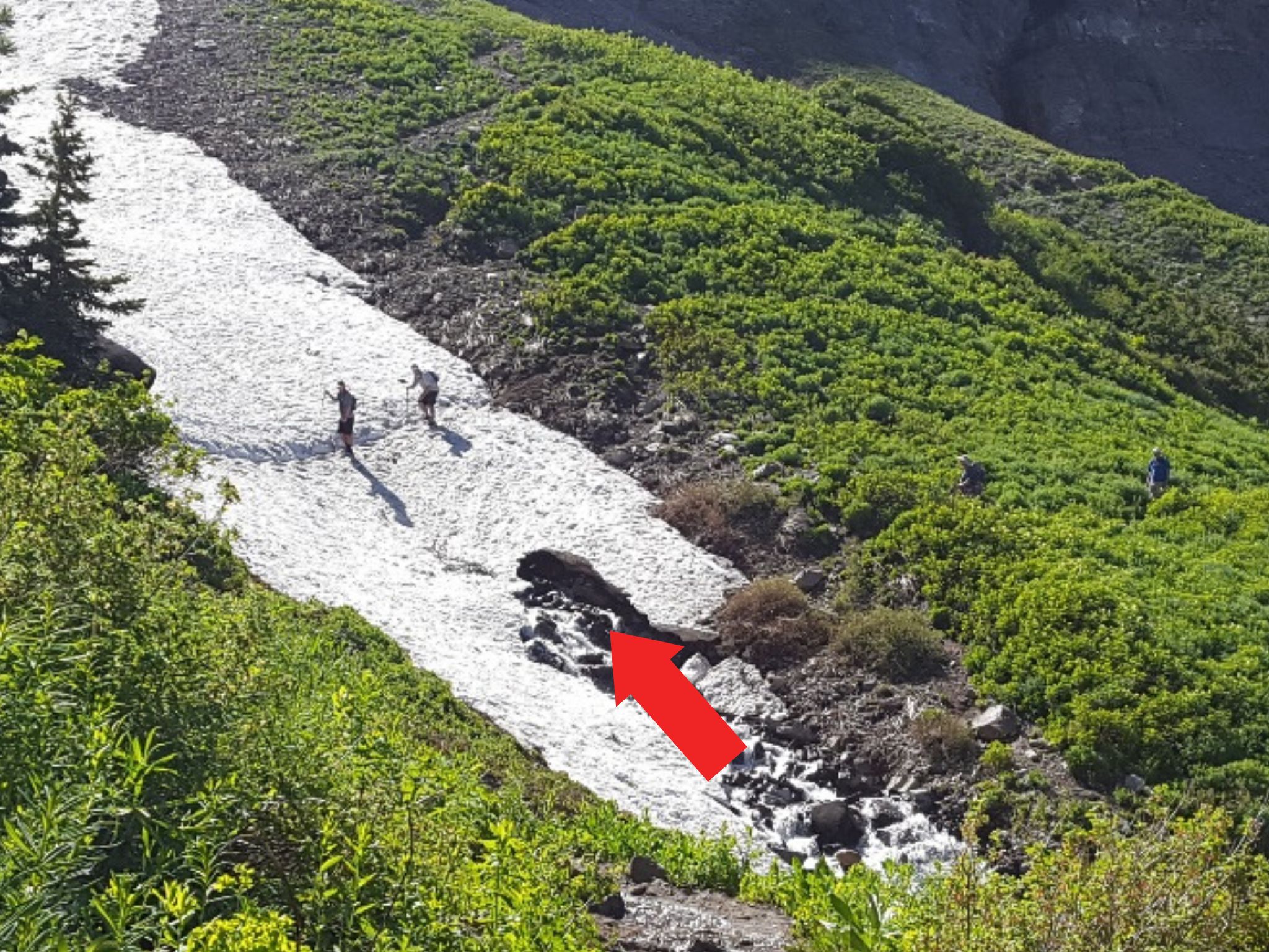 Several hikers are seen crossing a snowbridge